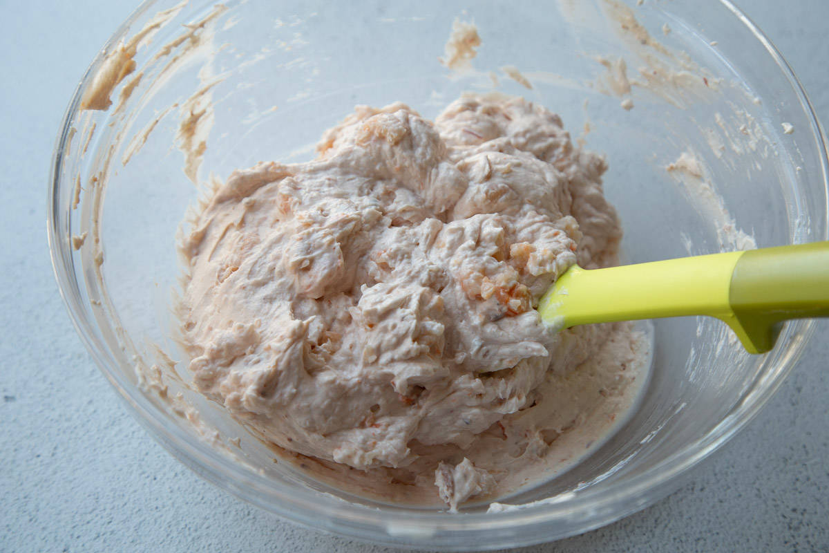 shrimp added to dip mix with a yellow spoon and clear glass mixing bowl.