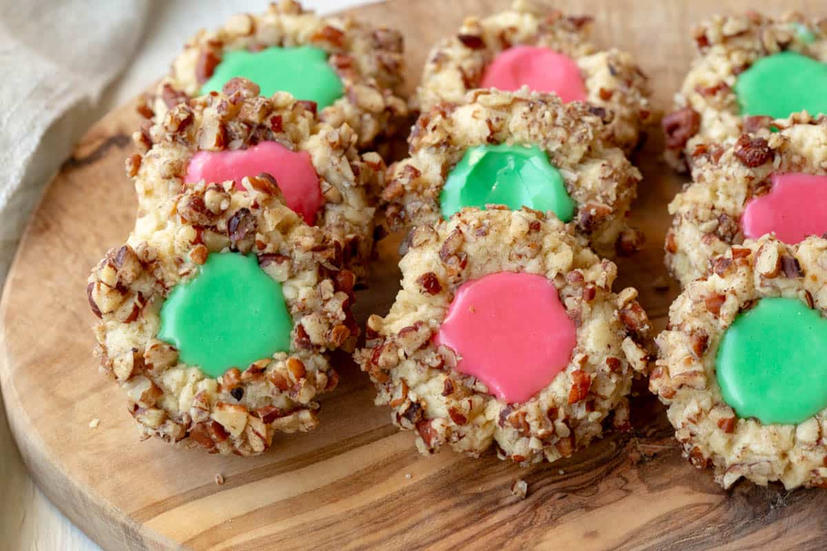 3 rows of thumbprint cookies with icing on a wooden cutting board.