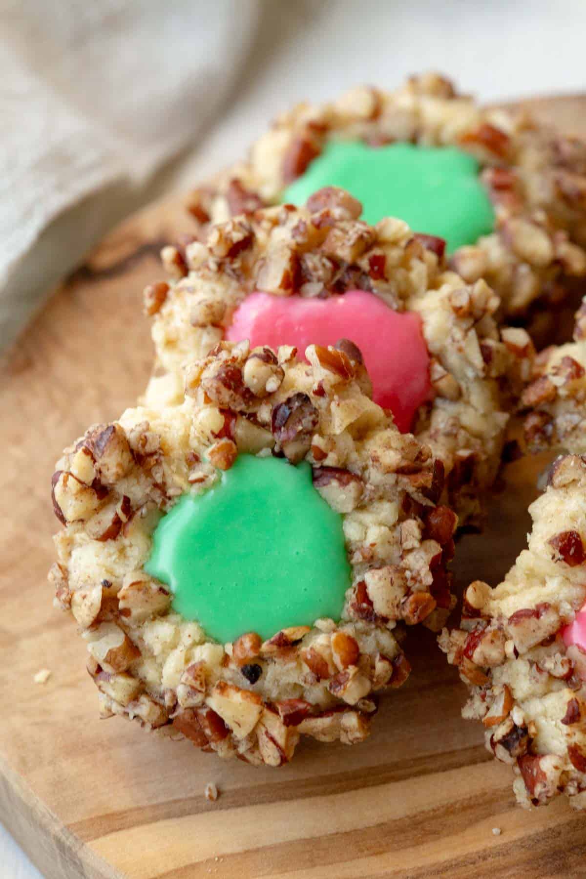 a row of 3 thumbprint cookies with icing on a wooden cutting board.