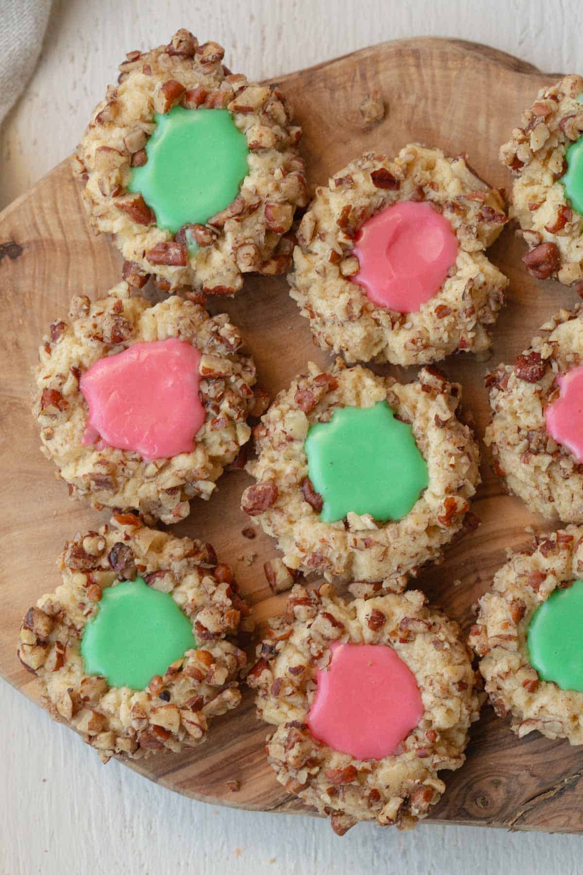 thumbprint cookies with icing placed side by side on a wooden cutting board.