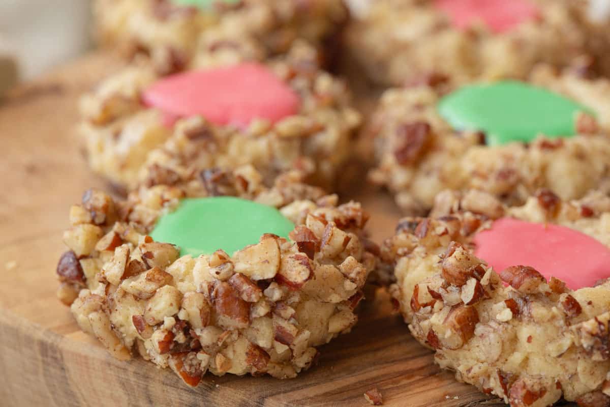 several thumbprint cookies with icing on a wooden cutting board.