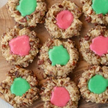 the top of several thumbprint cookies with icing on a wooden cutting board.