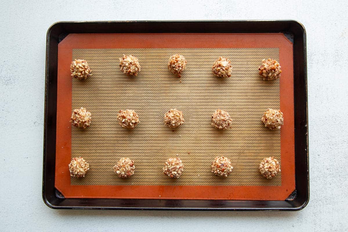 rolled and crusted thumbprint cookies on a silicone covered baking sheet.