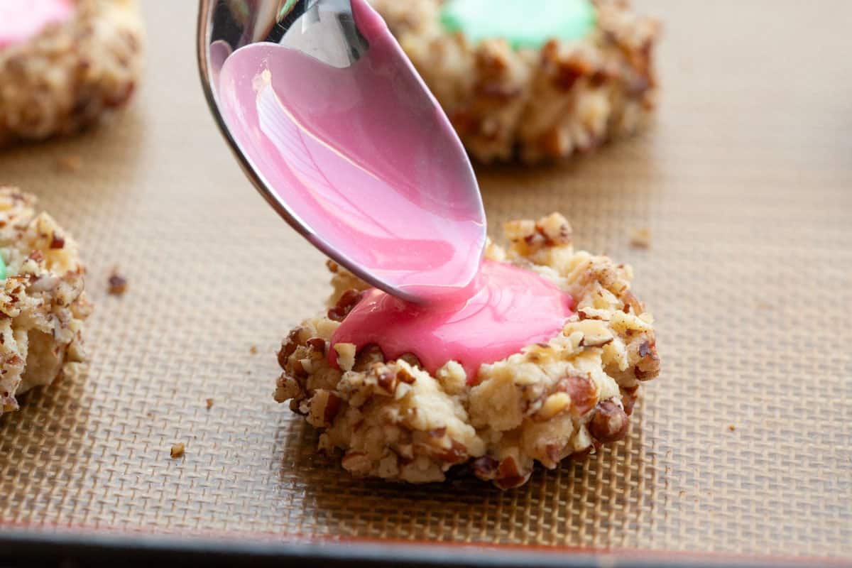 spoon pouring icing into the indentation on a thumbprint cookie.