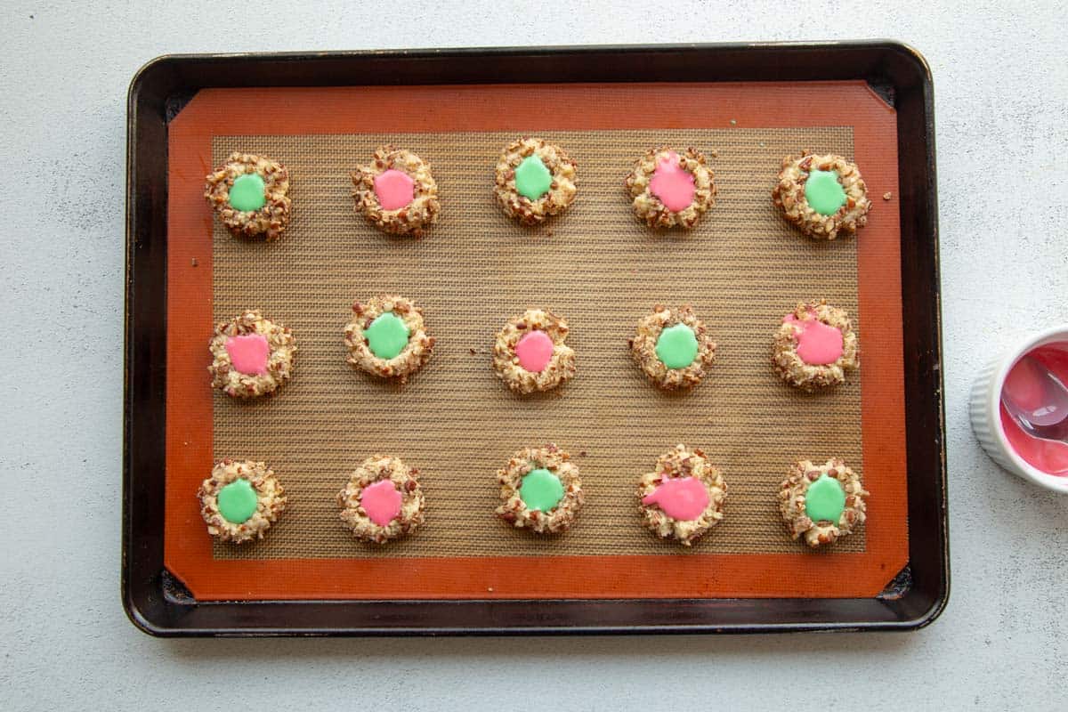 15 baked and iced thumbprint cookies on a baking sheet.