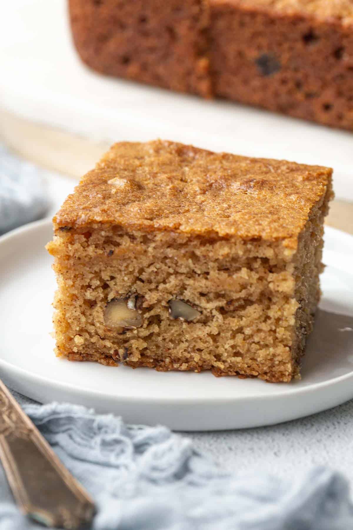 slice of applesauce cake on a white plate next to a fork.