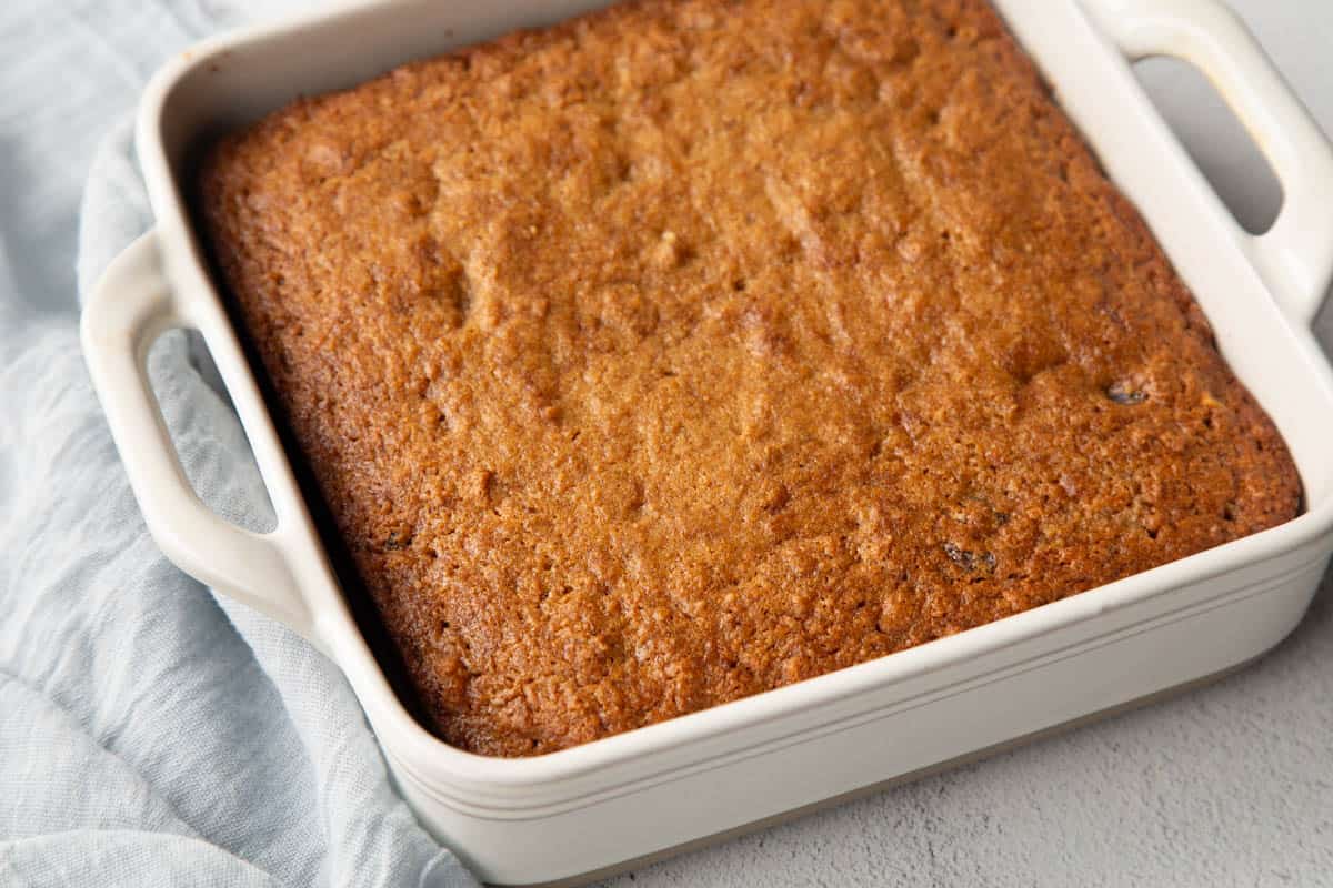 golden brown applesauce cake in a white dish with handles.