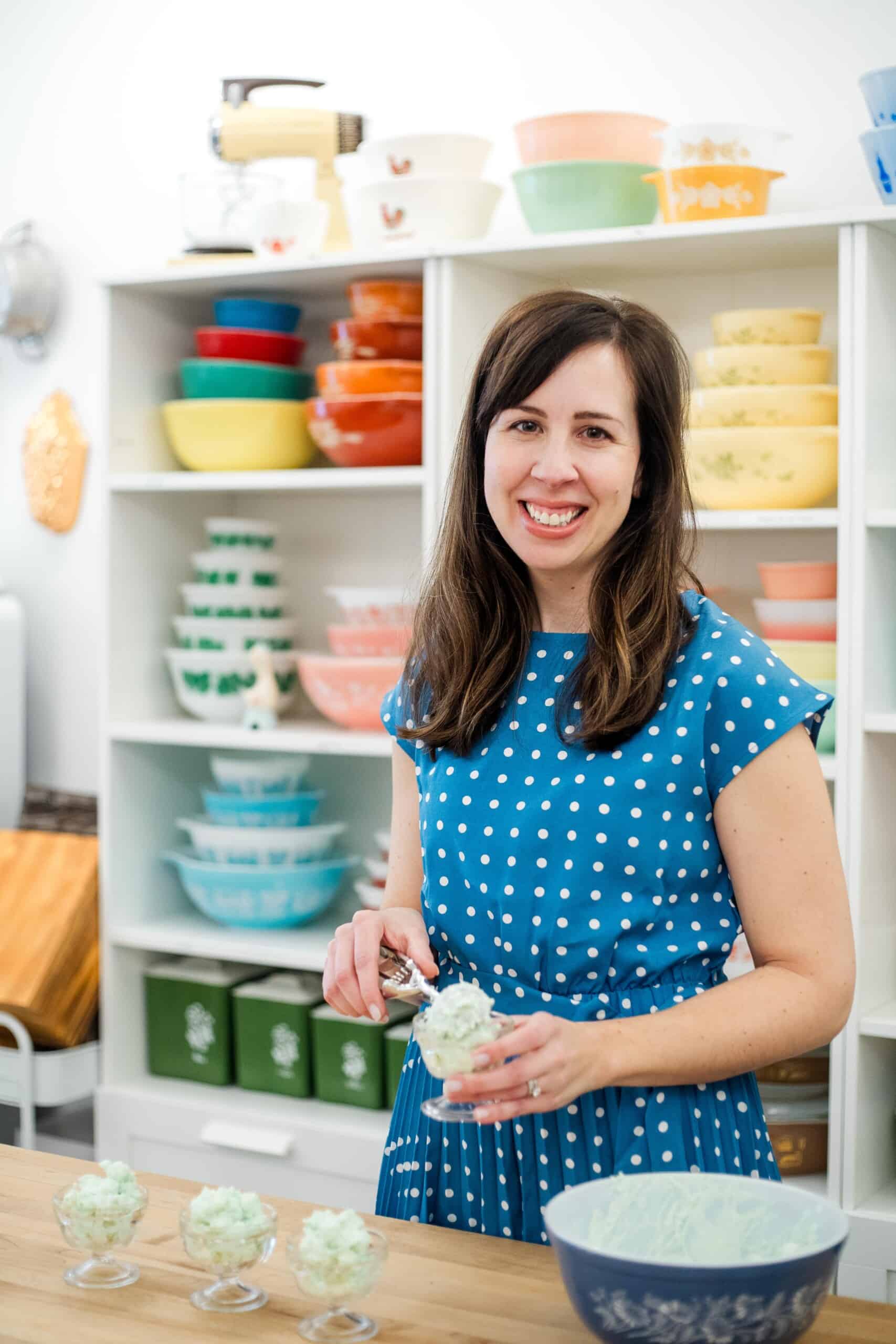 woman scooping pistachio salad into a parfait dish, with colorful vintage bowls in the background.