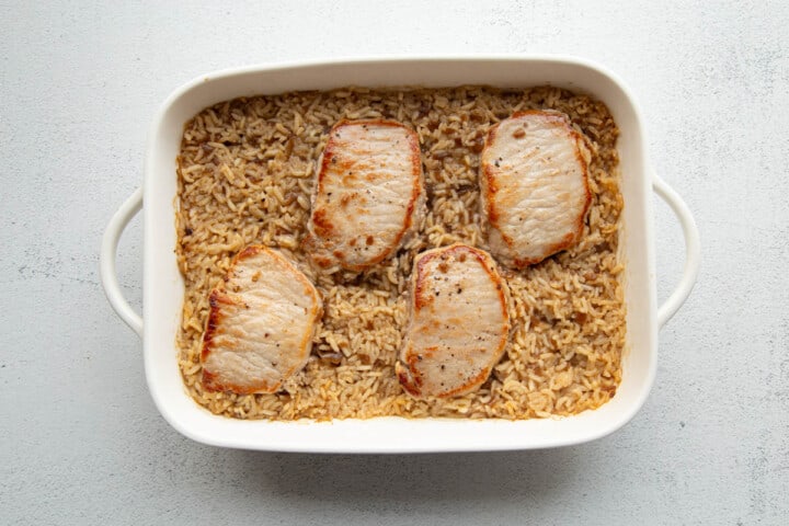 pork chops nestled in rice in a white casserole dish.