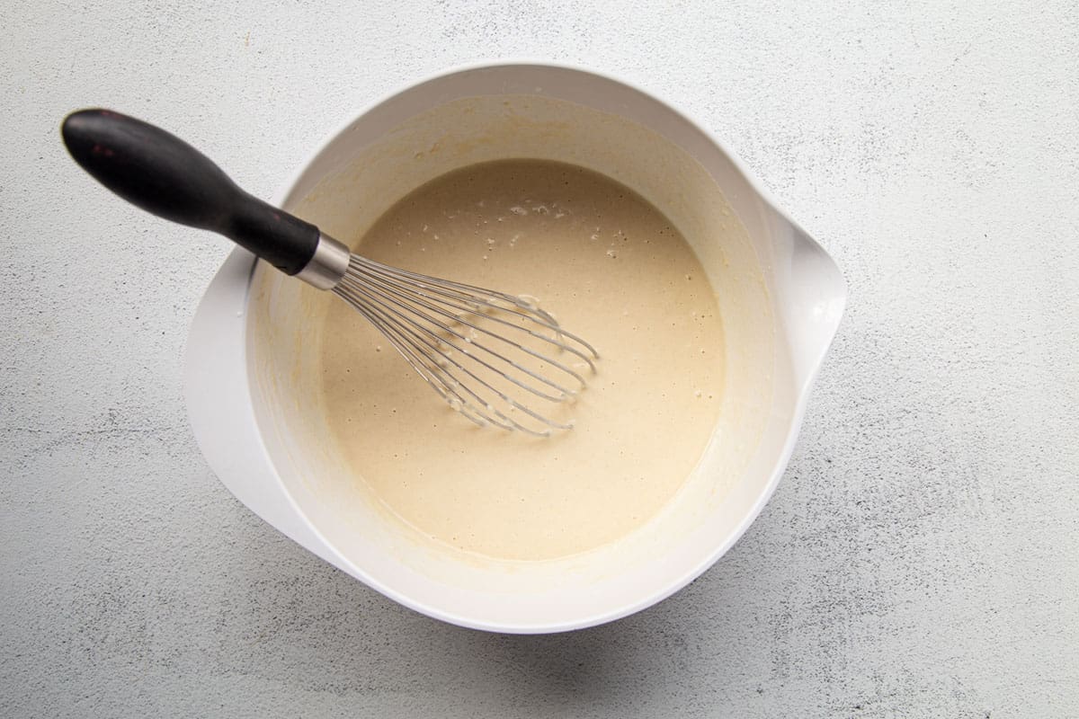 cream colored batter in a white bowl with a whisk.