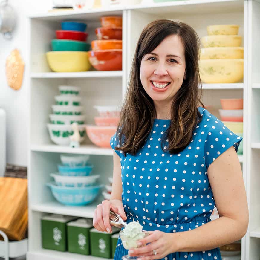 woman scooping pistachio salad into a parfait dish, with colorful vintage bowls in the background.