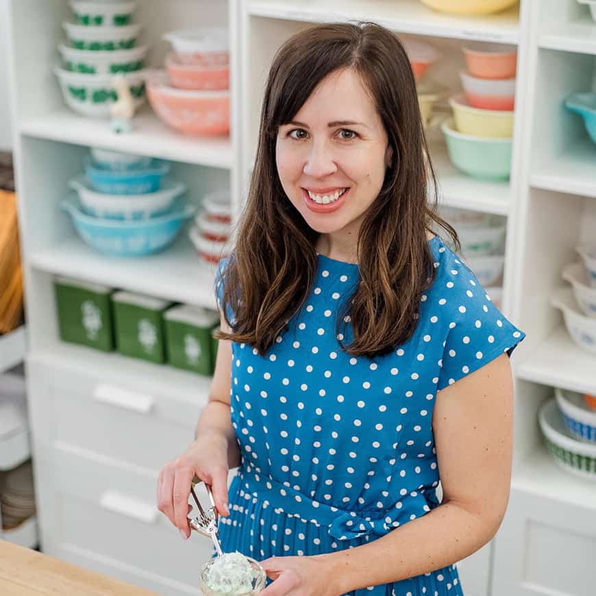 woman scooping with an ice cream scoop in front of a display of colorful vintage bowls.