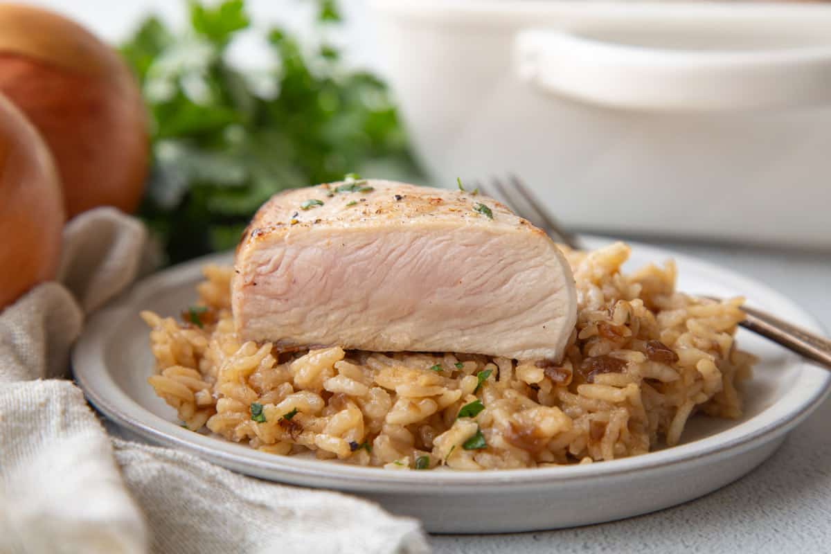 pork chop cut open with a blush of pink inside, sitting on top of oniony rice on a white plate.