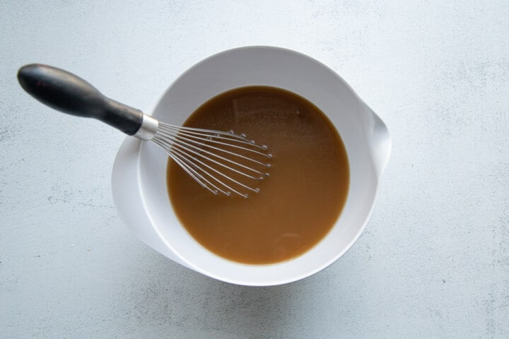 white bowl with a whisk filled with french onion soup and water.