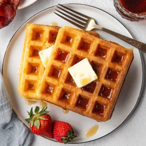 two yeasted belgian waffles on a plate with a pat of butter and maple syrup.