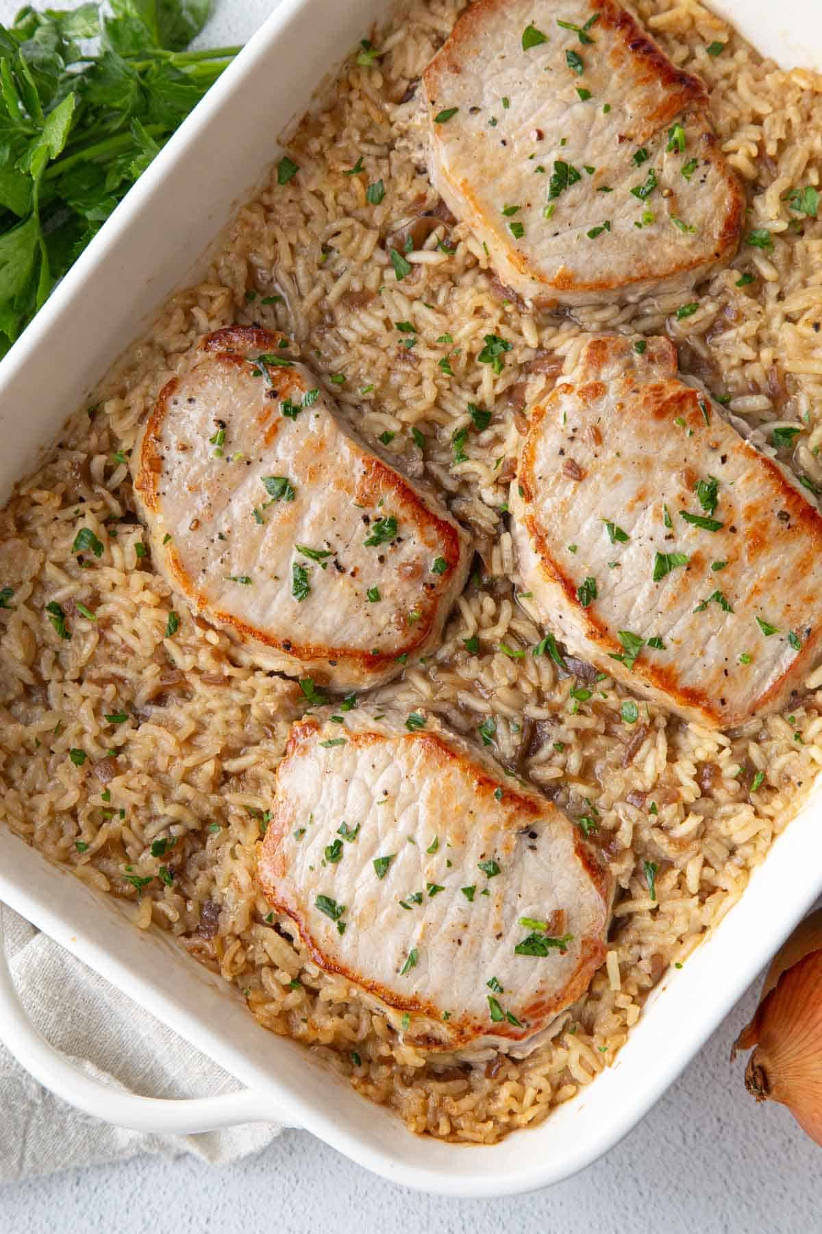 pork chops and rice casserole in a white dish, topped with parsley.