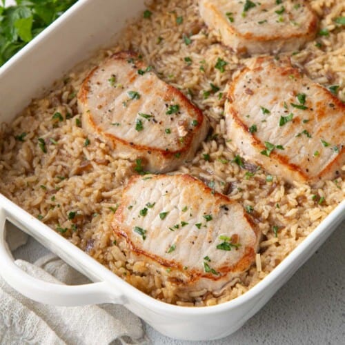 seared pork chops and rice in a white casserole dish.