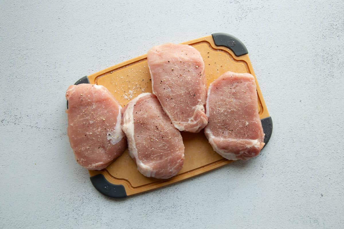 four raw pork chops on a brown cutting board.