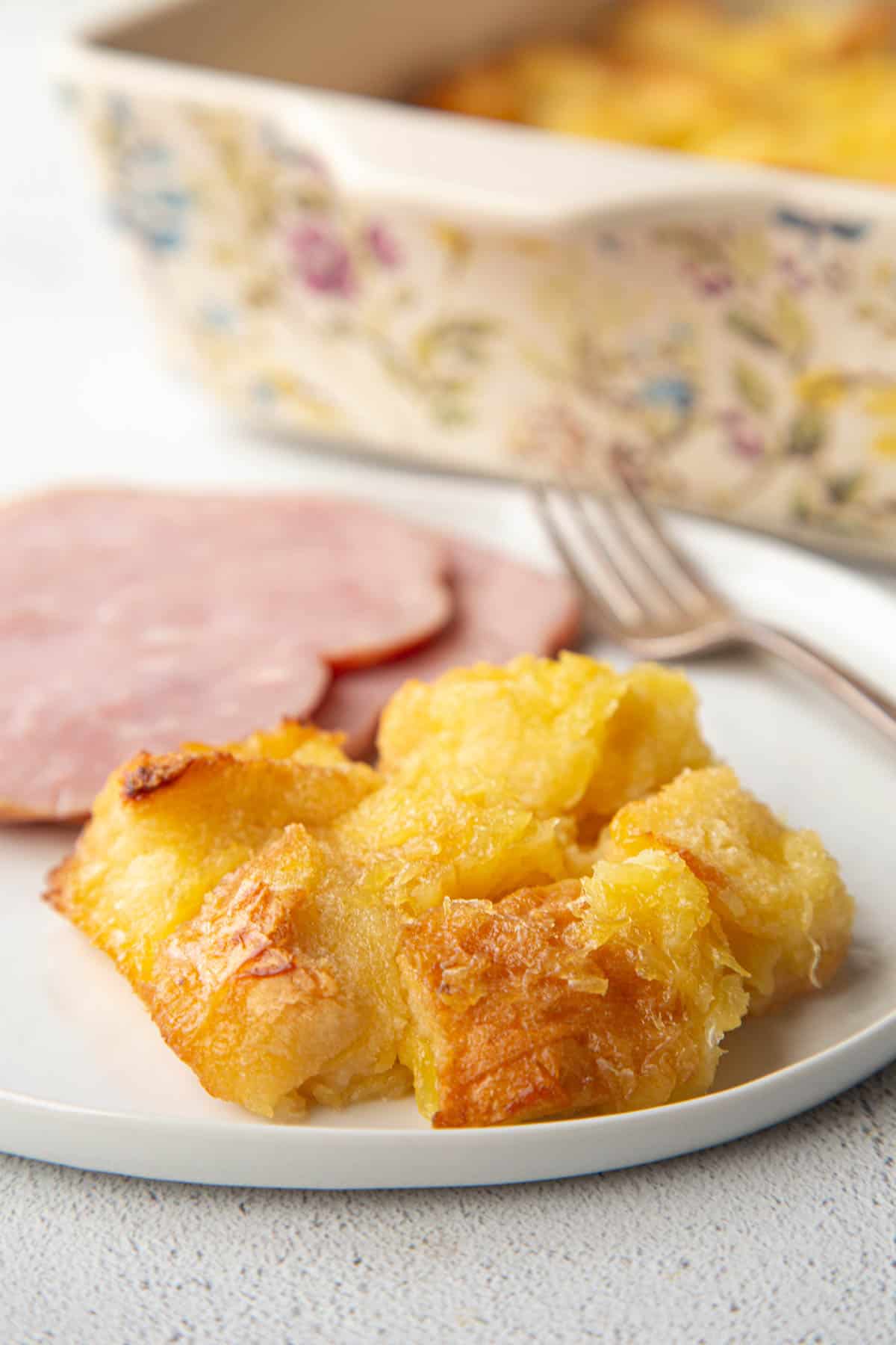 serving of scalloped pineapple on a plate with two ham slices.