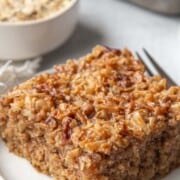slice of oatmeal cake with a crunchy coconut topping on a white plate.