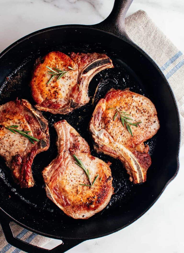 four bone-in pork chops in a skillet with rosemary sprigs.