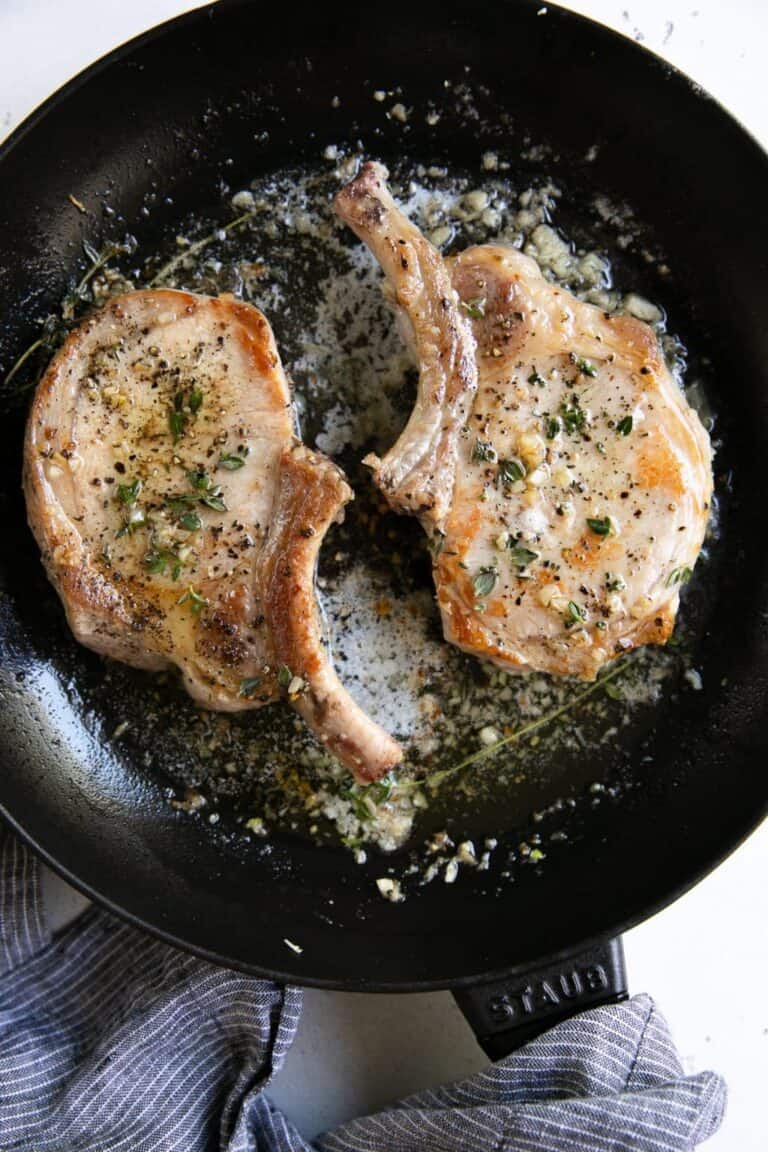 two bone-in pork chops in a frying pan with garlic butter.