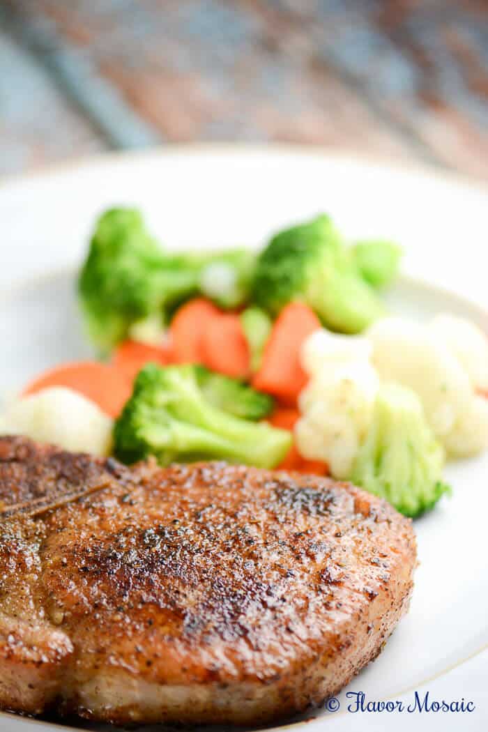 a seasoned pork chops on a plate with steamed veggies.