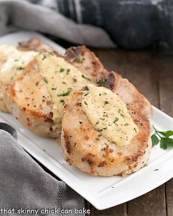 3 pork chops covered with dijonnaise sauce on a white platter.