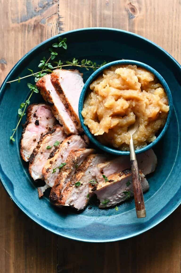 sliced pork chops on a blue plate next to a bowl of applesauce.