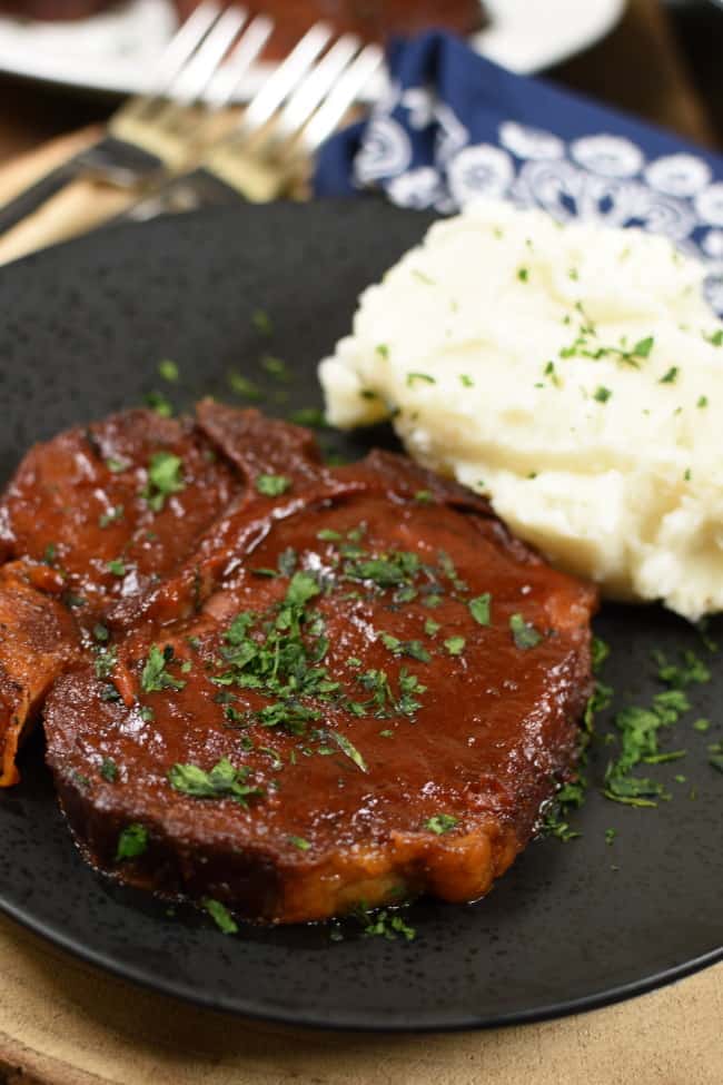 2 BBQ pork chops on a black plate next to a pile of mashed potatoes.