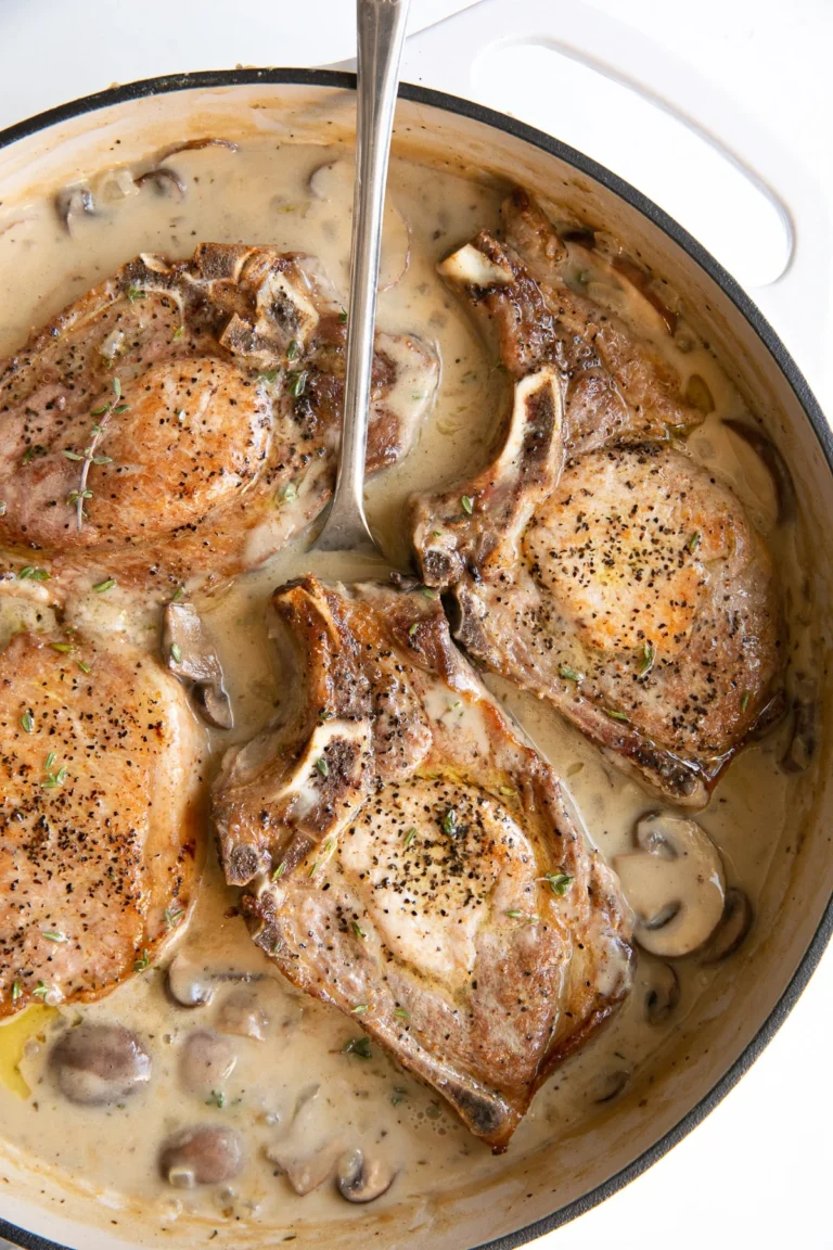 four smothered pork chops in a baking dish with a spoon inserted into the sauce.