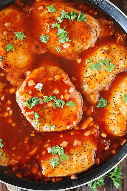 several pork chops in a pan simmering in sweet BBQ sauce.