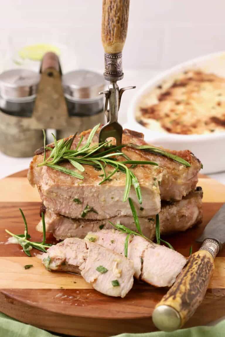 2 pork chops on a cutting board with slices removed and rosemary on top.