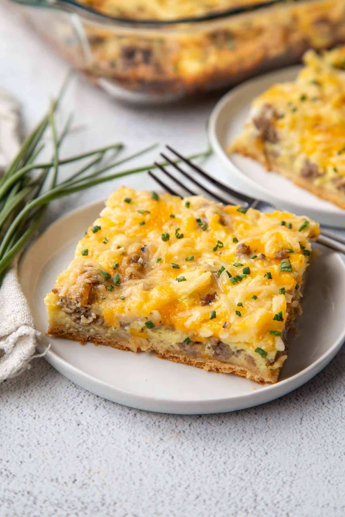 slice of breakfast pizza with sausage on a white plate.