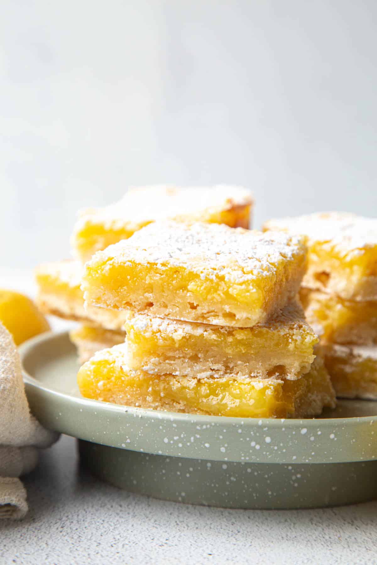 pile of lemon bars with shortbread crust on a green cake pedestal.