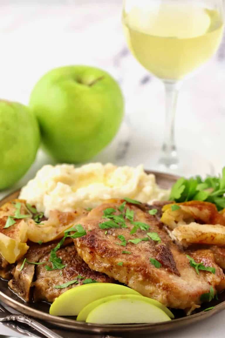 pork chops with apples on a plate next to a scoop of mashed potatoes.