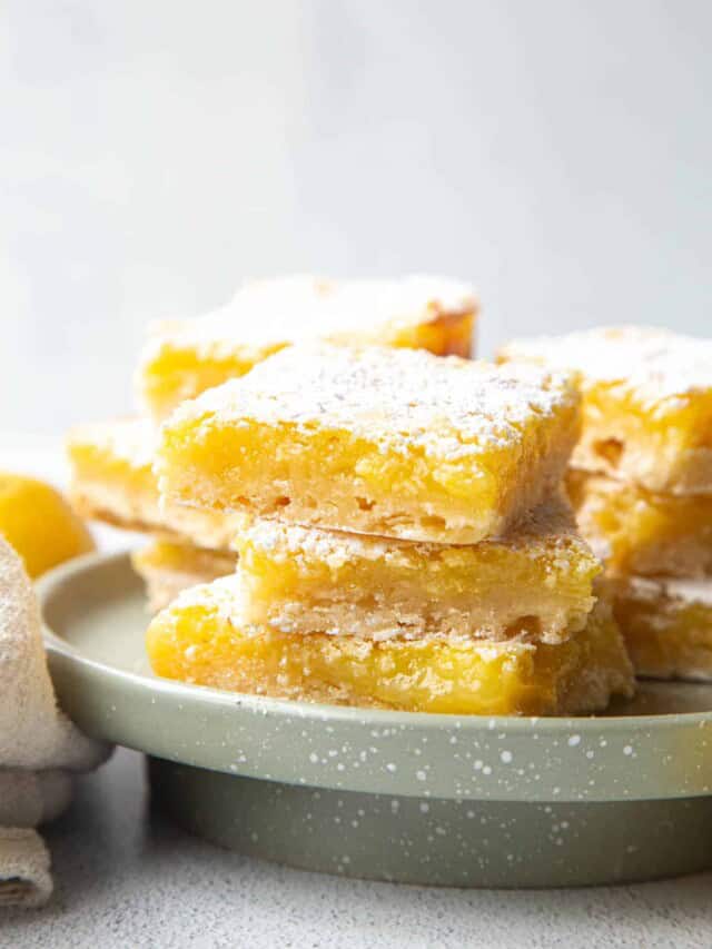 pile of lemon bars with shortbread crust on a green cake pedestal.