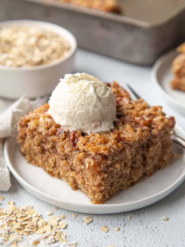 oatmeal cake slice on a white plate, topped with a scoop of vanilla ice cream.