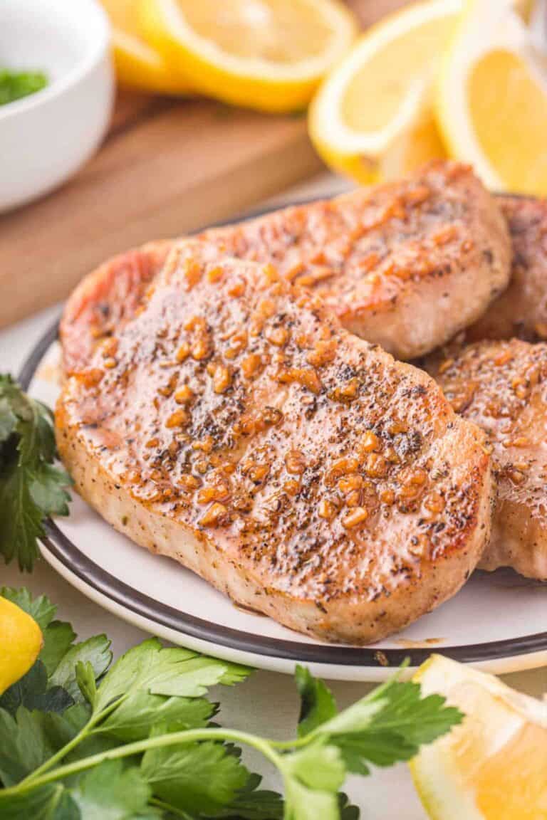 several honey garlic pork chops on a plate next to parsley and lemons.