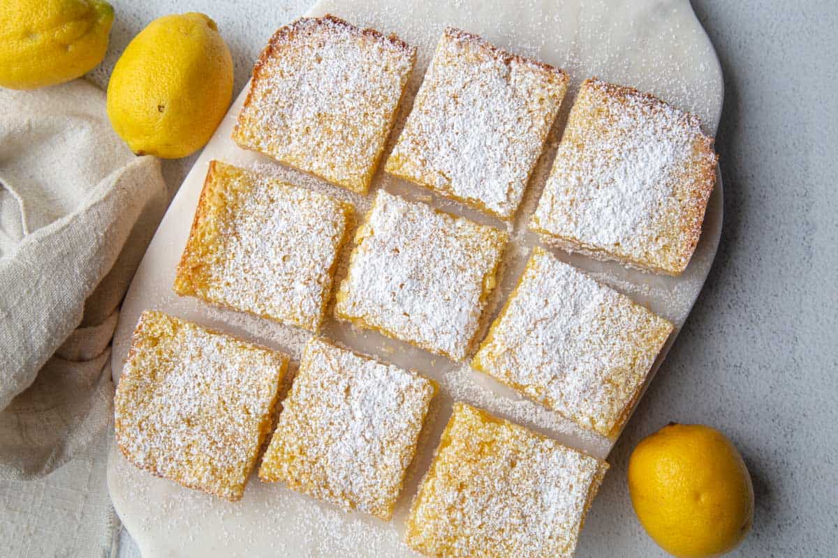 9 lemon bars topped with powdered sugar on a white marble board.
