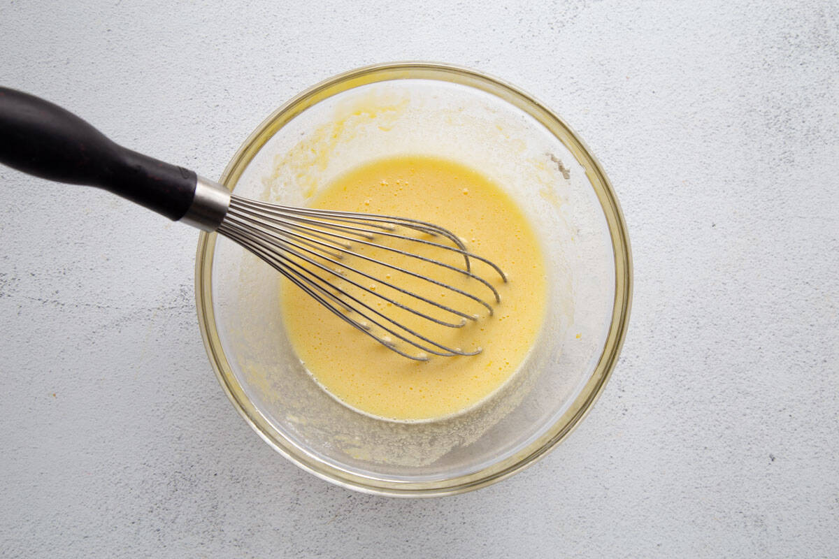 glass mixing bowl filled with a lemon mixture and a whisk.