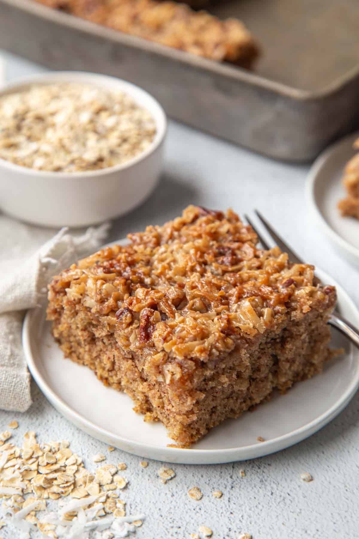 slice of old fashioned oatmeal cake on a white plate with a cup of oats in the background.