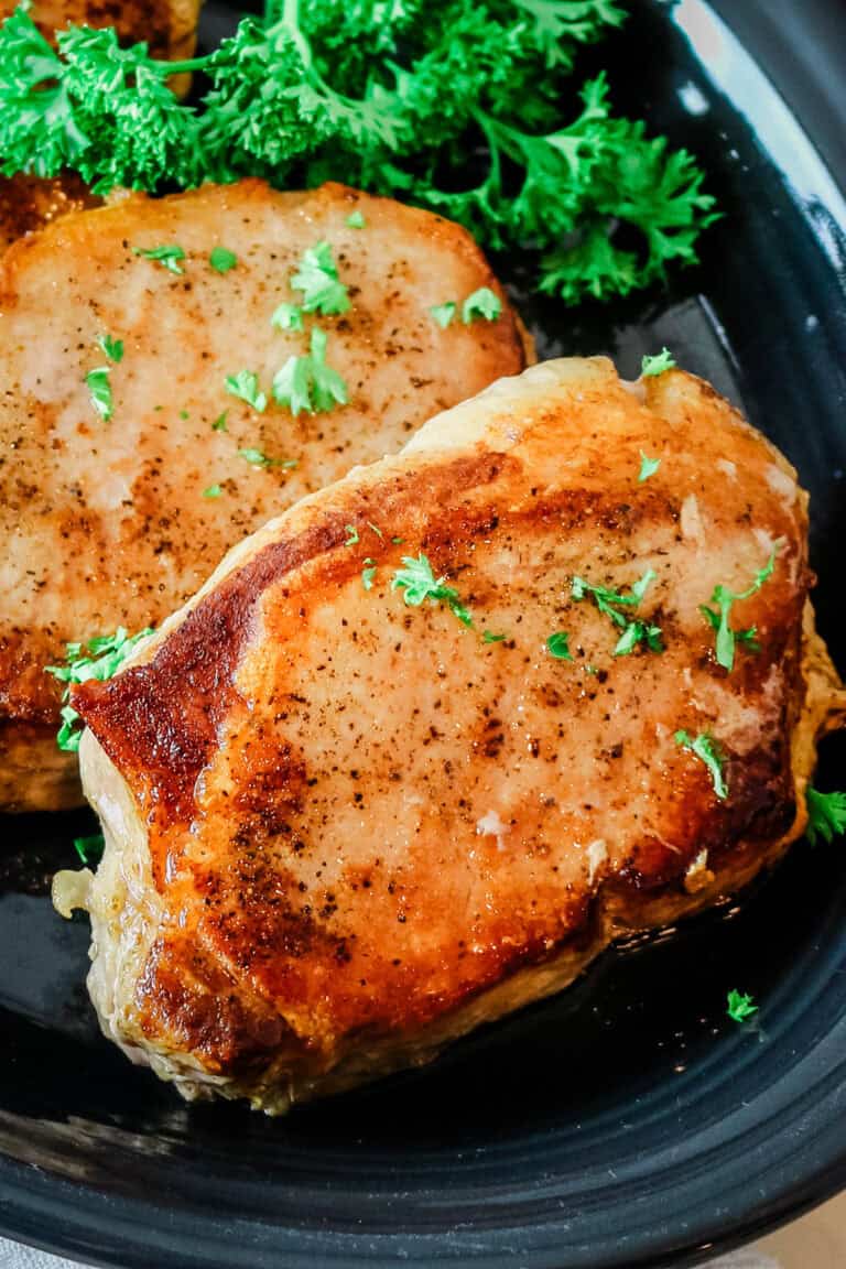 two pan-seared pork chops on a black plate.