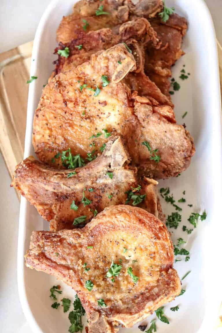 several fried pork chops sprinkled with parsley on white serving platter.
