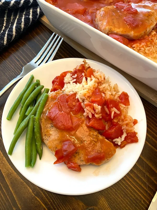 a serving of pork chop casserole with tomato gravy on a white plate next to green beans.
