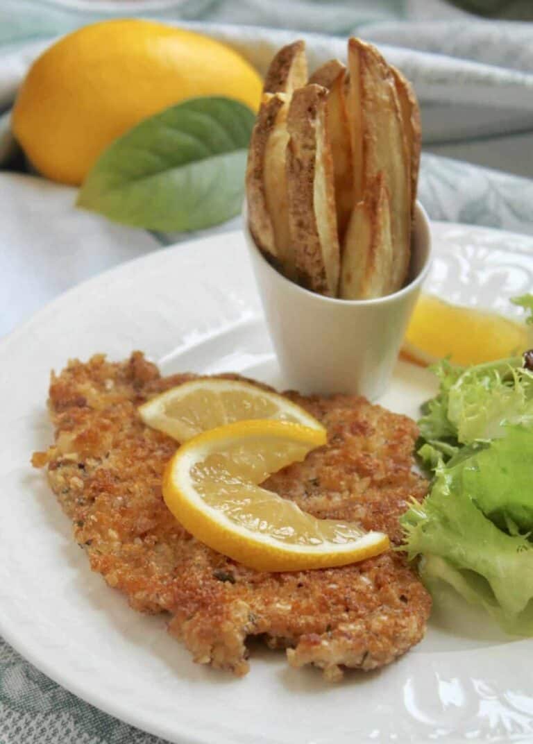 a pork schniztel cutlet on a plate with lemon, salad, and fries.
