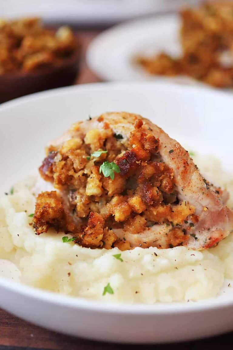 a stuffed pork chop on a bed of mashed potatoes on a white plate.