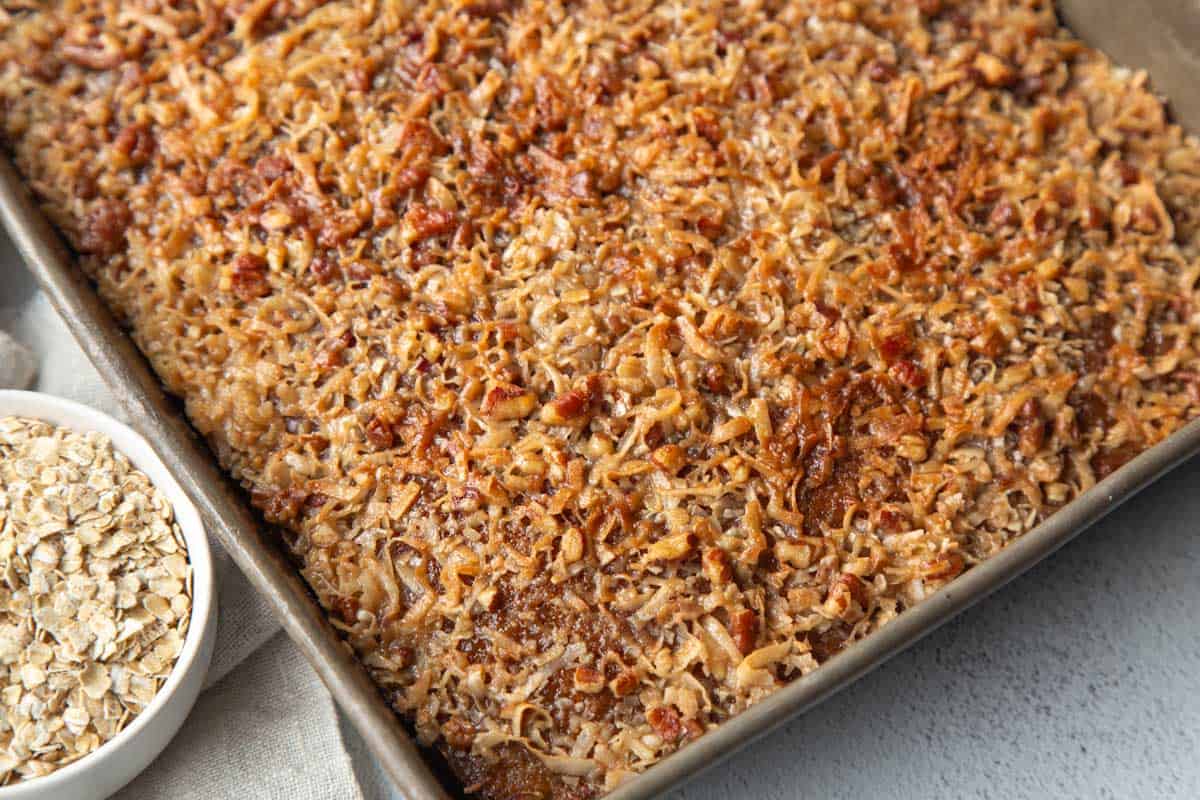 whole oatmeal cake topped with pecans and coconut in a metal pan.