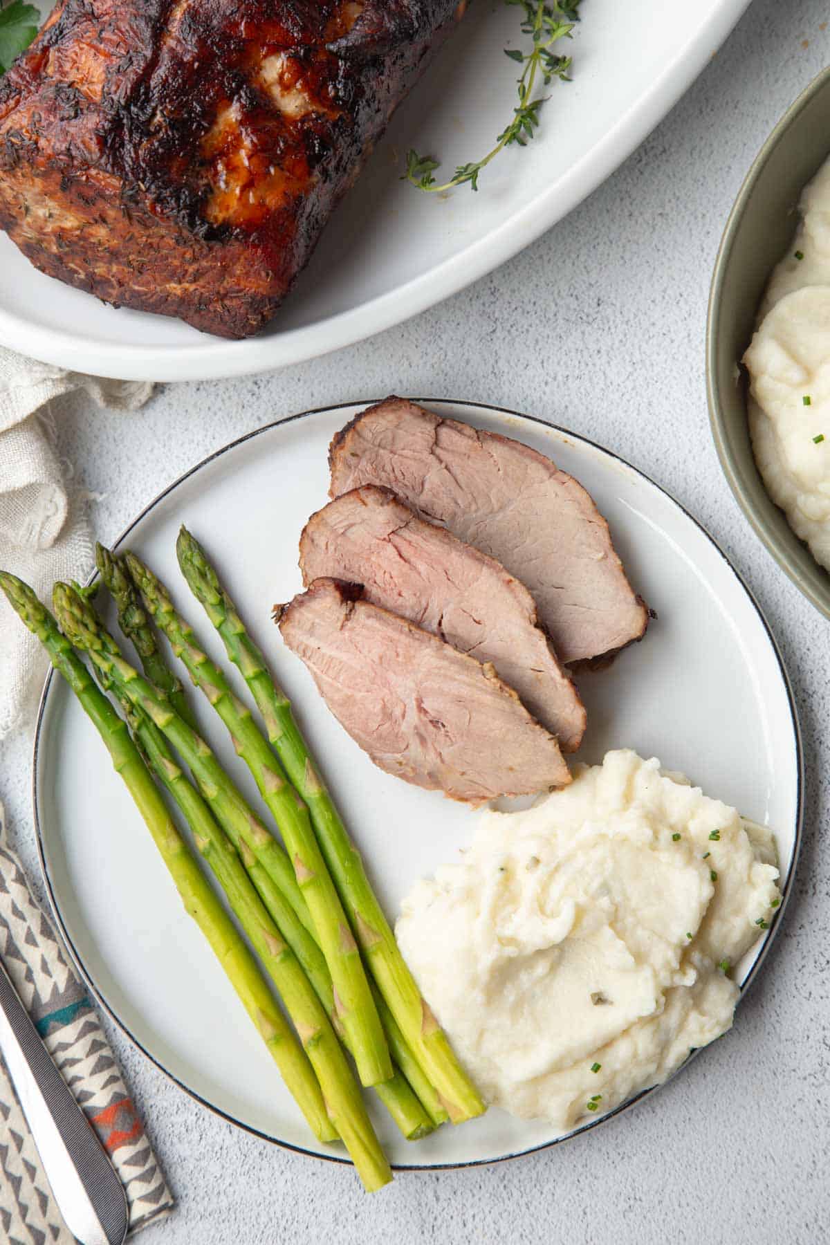 dinner plate with pork slices, mashed potatoes, and asparagus.