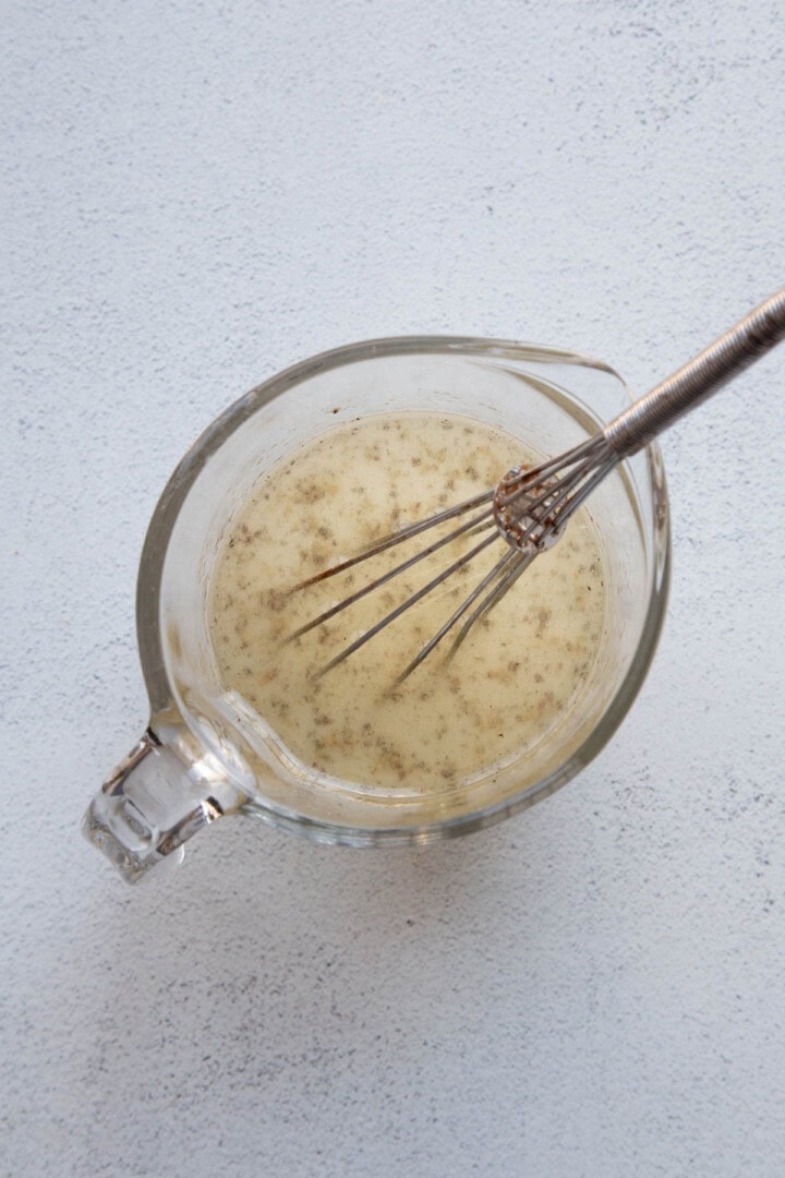 vinaigrette in a glass measuring cup with a whisk in it.
